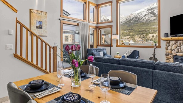 A dining area with a wooden table, chairs, and a vase of flowers. - Lady Mac Hydeaway at the Crossing (Canmore)