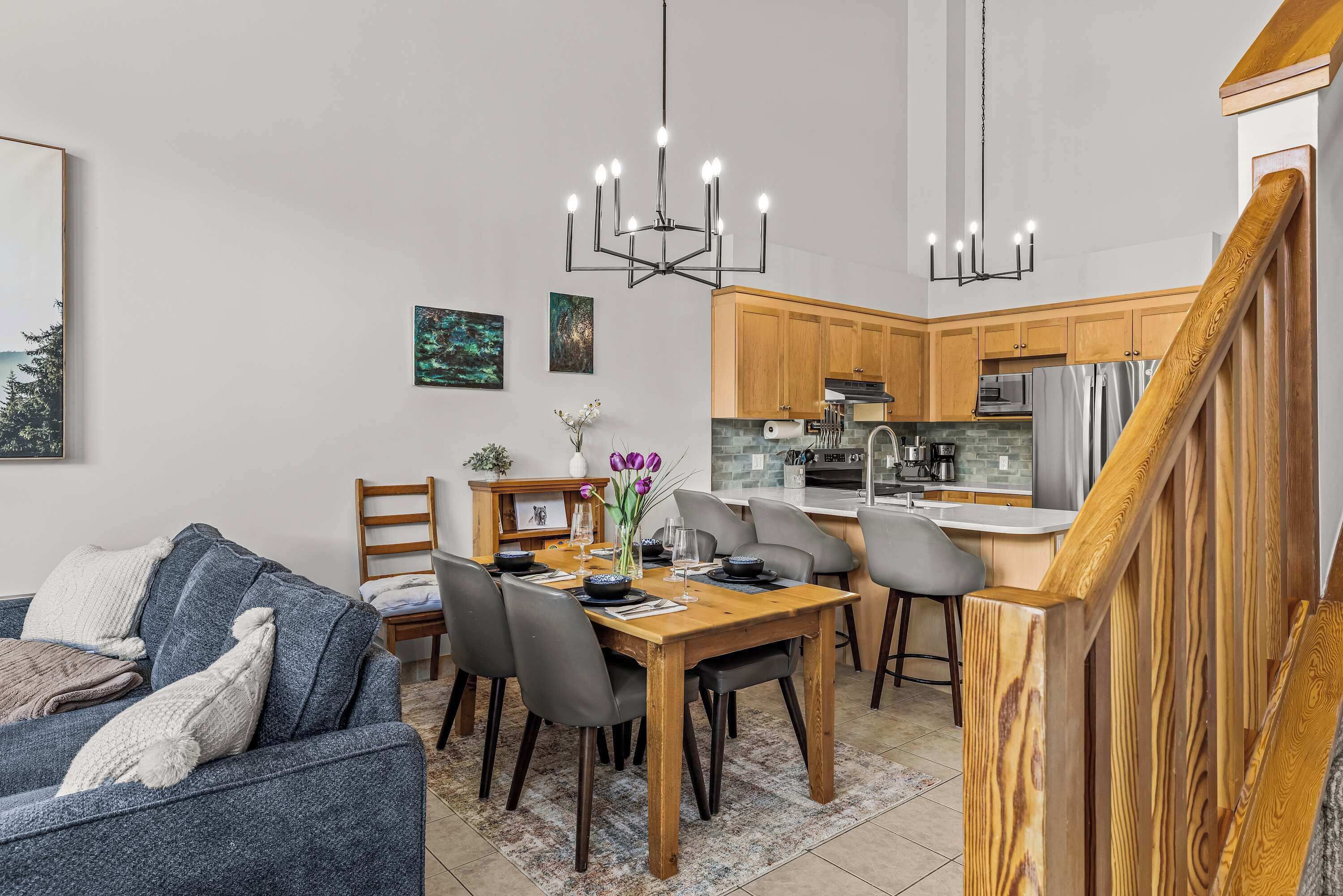 A modern kitchen with wooden cabinets, a dining table with chairs, and a chandelier.