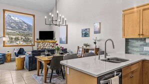 A modern kitchen with a large island, a dining area with a stone fireplace, and a living room with a mountain view. - Lady Mac Hydeaway at the Crossing (Canmore)