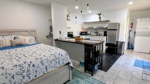 Une chambre moderne avec un grand lit, un coin cuisine équipé d’un four à micro-ondes, d’un réfrigérateur et d’un évier, ainsi qu’une petite table à manger.