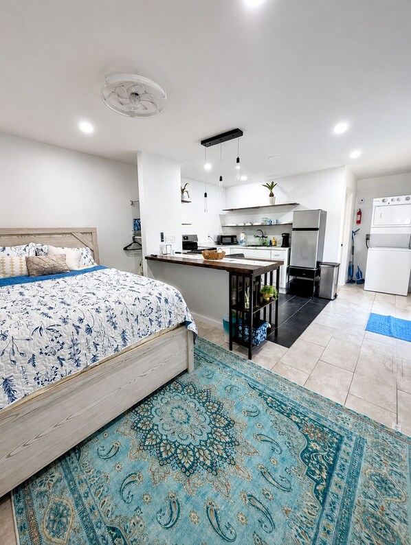 Ein modernes Schlafzimmer mit einem großen Bett, einer kleinen Küchenzeile mit Kühlschrank und einem Badezimmer mit Dusche.