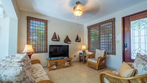 A living room with a television, wicker furniture, and decorative wall sconces. - Private Home Pool Ocean Views Walk to Beach (Rincon)
