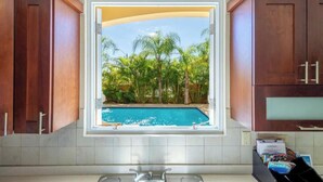 A kitchen with a window view of a swimming pool and palm trees. - Private Home Pool Ocean Views Walk to Beach (Rincon)