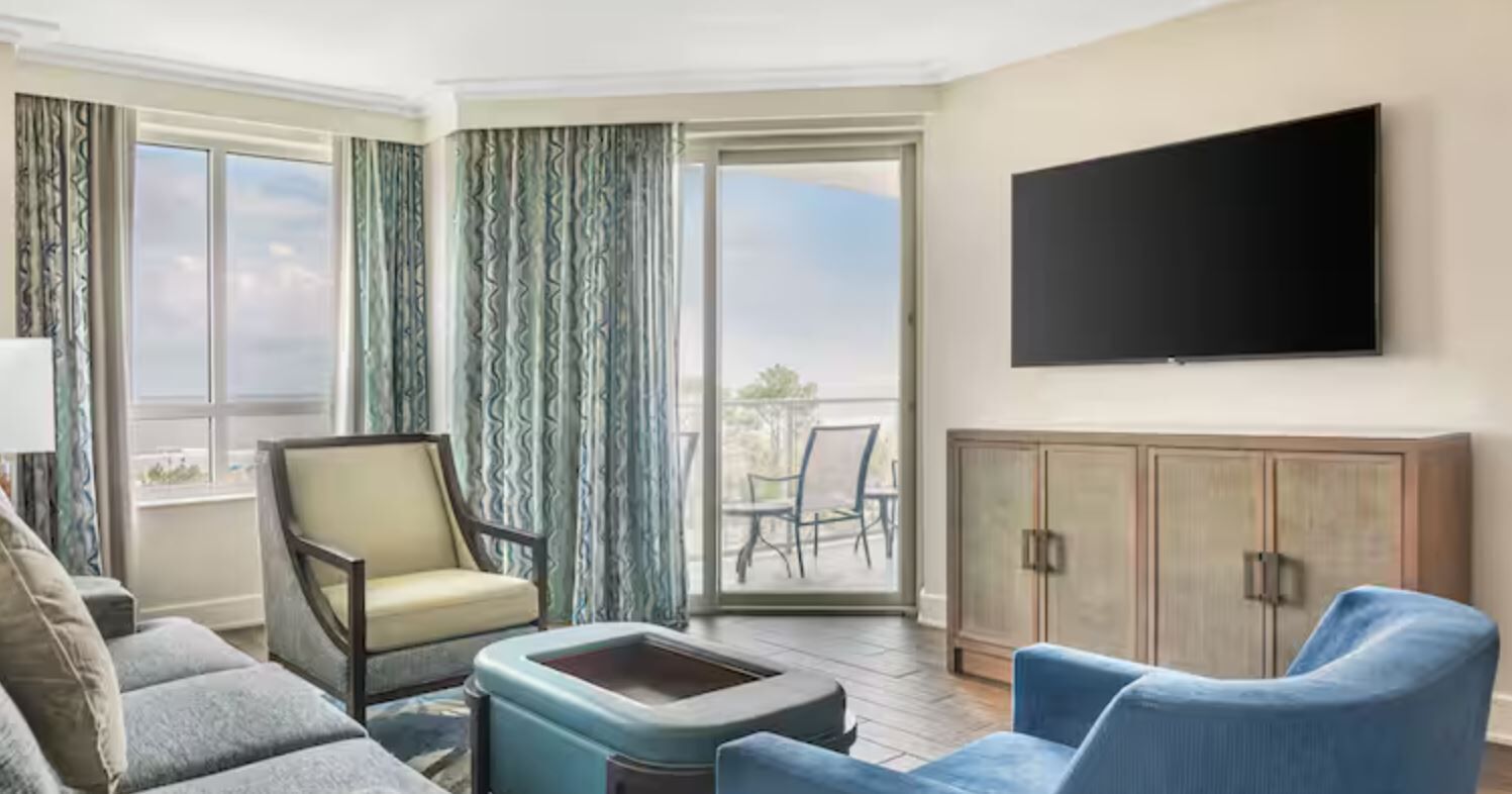 Habitación de hotel con sofá, sillón y televisor de pantalla plana montado en la pared.