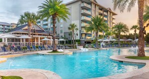 Un hôtel doté d’une piscine, de palmiers et de chaises longues.