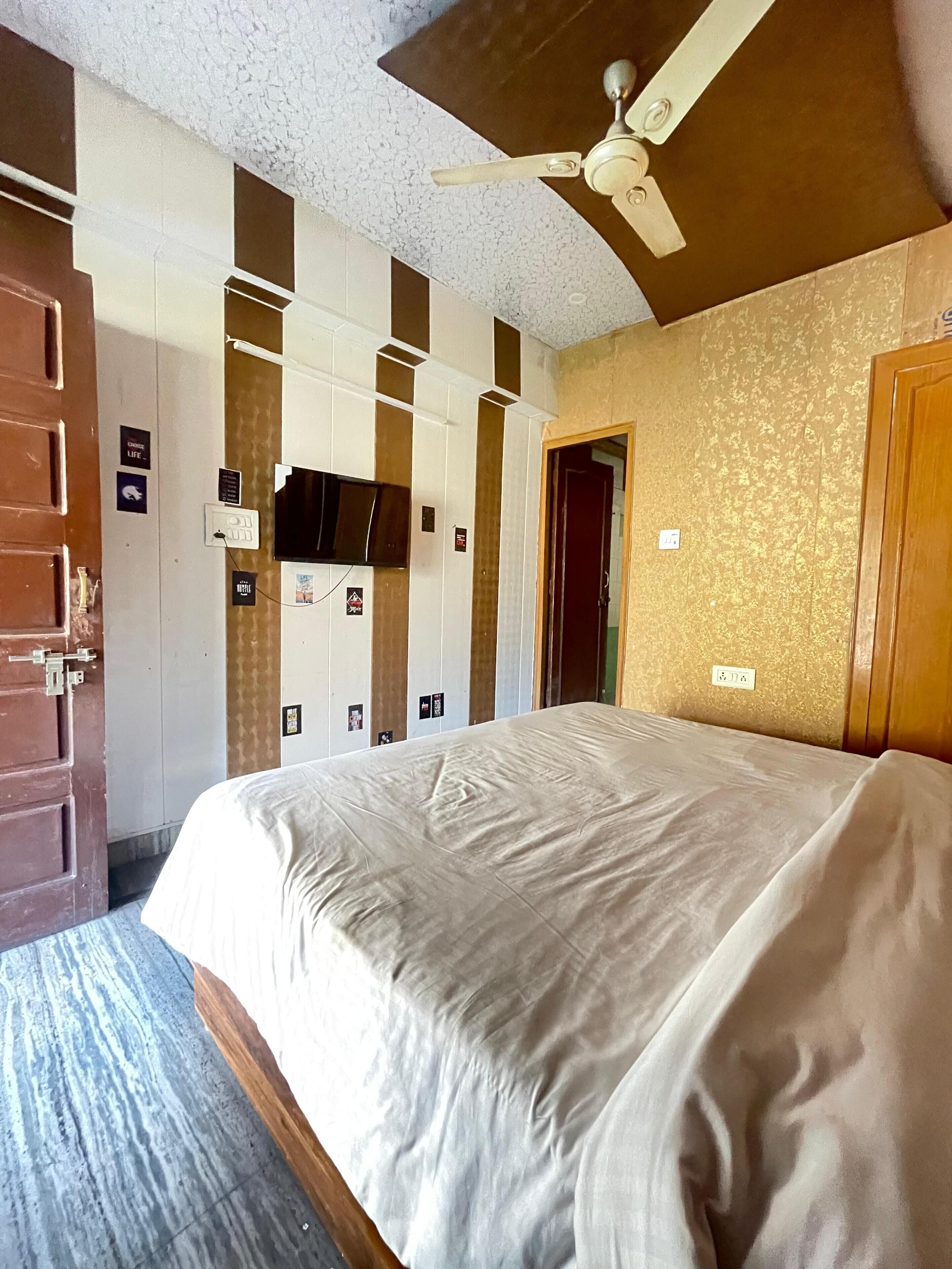 A hotel room with a bed, a ceiling fan, a door, and a wall with a patterned design.