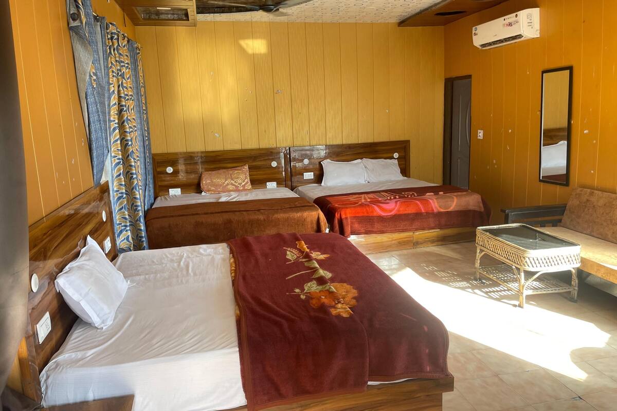 A room with two wooden beds, a bench, a small table, and an air conditioning unit.
