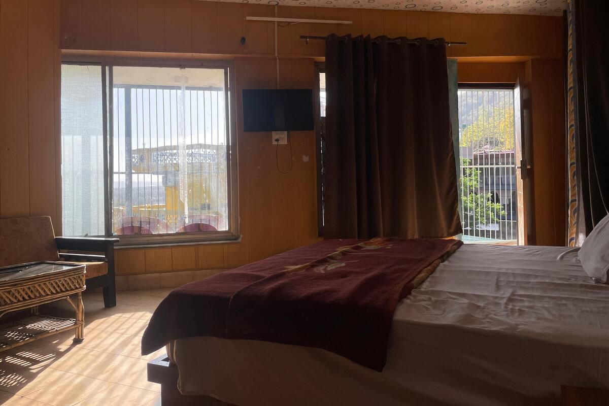 A hotel room with a bed, a chair, a window with a view, a ceiling fan, and curtains.