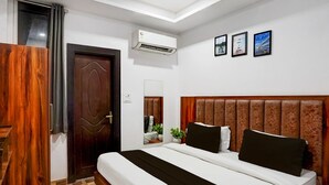 A bedroom with a bed, a wooden door, an air conditioning unit, and framed pictures on the wall. - Hotel Elevate Nirvana (Rishikesh)