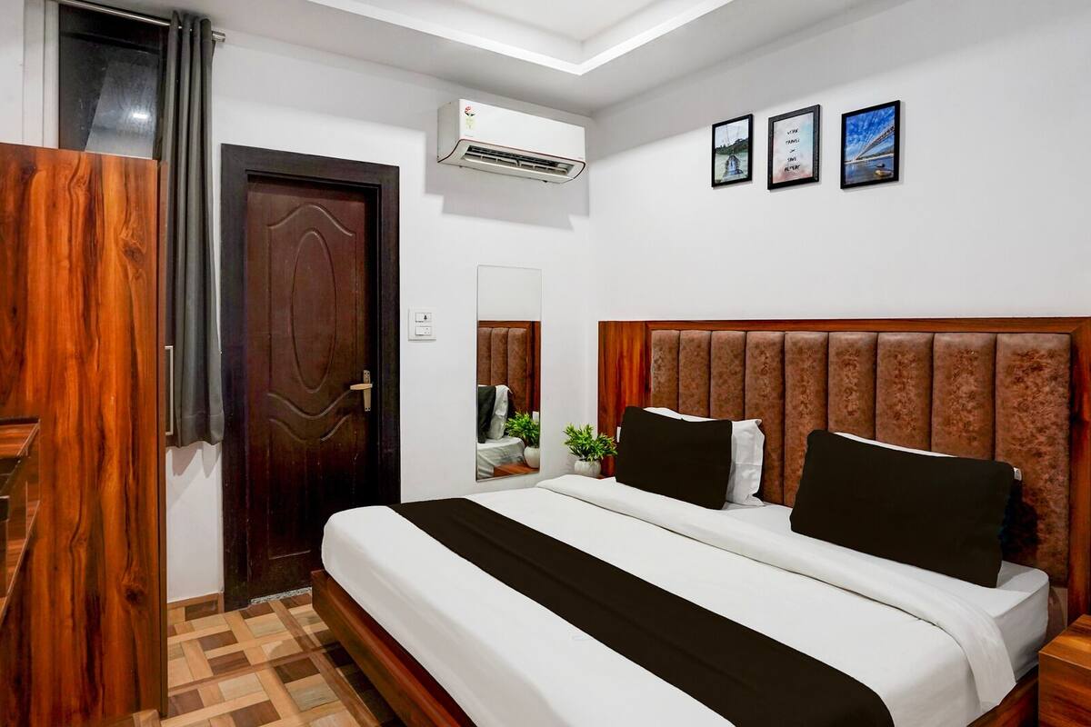 A bedroom with a bed, a wooden door, an air conditioning unit, and framed pictures on the wall.