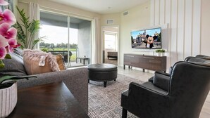 Un salon moderne avec un canapé, un pouf et un téléviseur à écran plat posé sur un meuble.