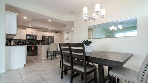 Une cuisine moderne avec des meubles blancs, une table à manger avec des chaises et un lustre.