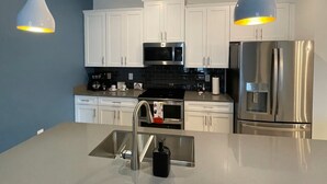 A modern kitchen with white cabinets, stainless steel appliances, a black tiled backsplash, and pendant lighting. - Last Minute Disney Getaway! Private Pool & Themed Bedrooms. Book Now! #165355 (Orlando)