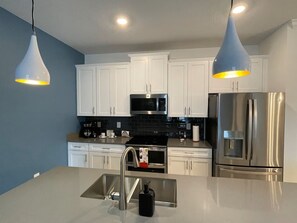 Une cuisine moderne avec des armoires blanches, des appareils en acier inoxydable, un dosseret de carreaux noirs et des luminaires suspendus.