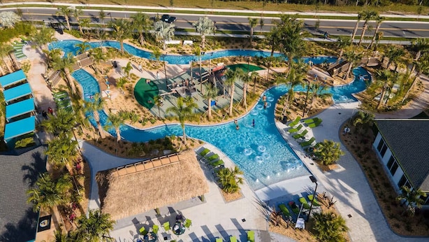 An aerial view of a resort with a winding pool, lounge areas, and a thatched-roof structure. - Last Minute Disney Getaway! Private Pool & Themed Bedrooms. Book Now! #165355 (Orlando)
