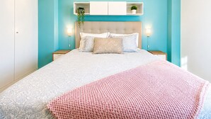 Un dormitorio con cama, mesitas de noche, cabecera y estante de pared con plantas.