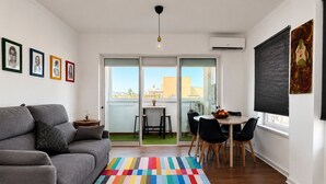 Una sala de estar moderna con un sofá gris, un tapete colorido a rayas, un comedor con mesa y sillas, y obras de arte en las paredes.