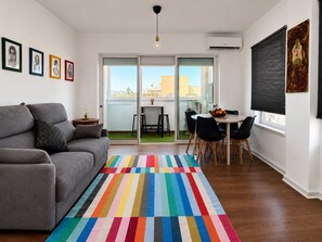 Ein modernes Wohnzimmer mit einem grauen Sofa, einem farbenfrohen Streifen Teppich, einem Essbereich mit Tisch und Stühlen sowie Kunstwerken an den Wänden.
