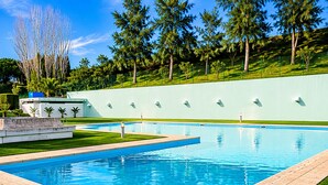 A rectangular swimming pool with a tiled deck, surrounded by a grassy area and a low wall with evenly spaced lights. - Lisbon Luxury T1: Free Pool, Tennis, Gym, Game Room & Parking (Lisboa)