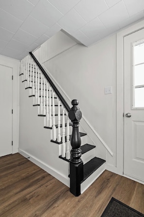 A staircase with white balusters and black handrails, leading to a landing with a white door and a window.