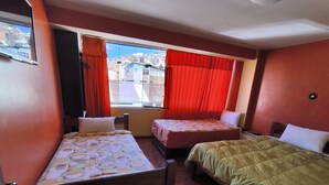 Una habitación con dos camas, una ventana con cortinas rojas y vistas a edificios.