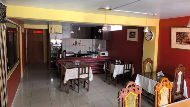 Comedor con cocina al fondo, un reloj en la pared y una puerta con luz roja.