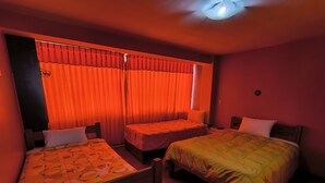 Habitación de hotel con dos camas individuales, una mesita y un ventanal con cortinas rojas.