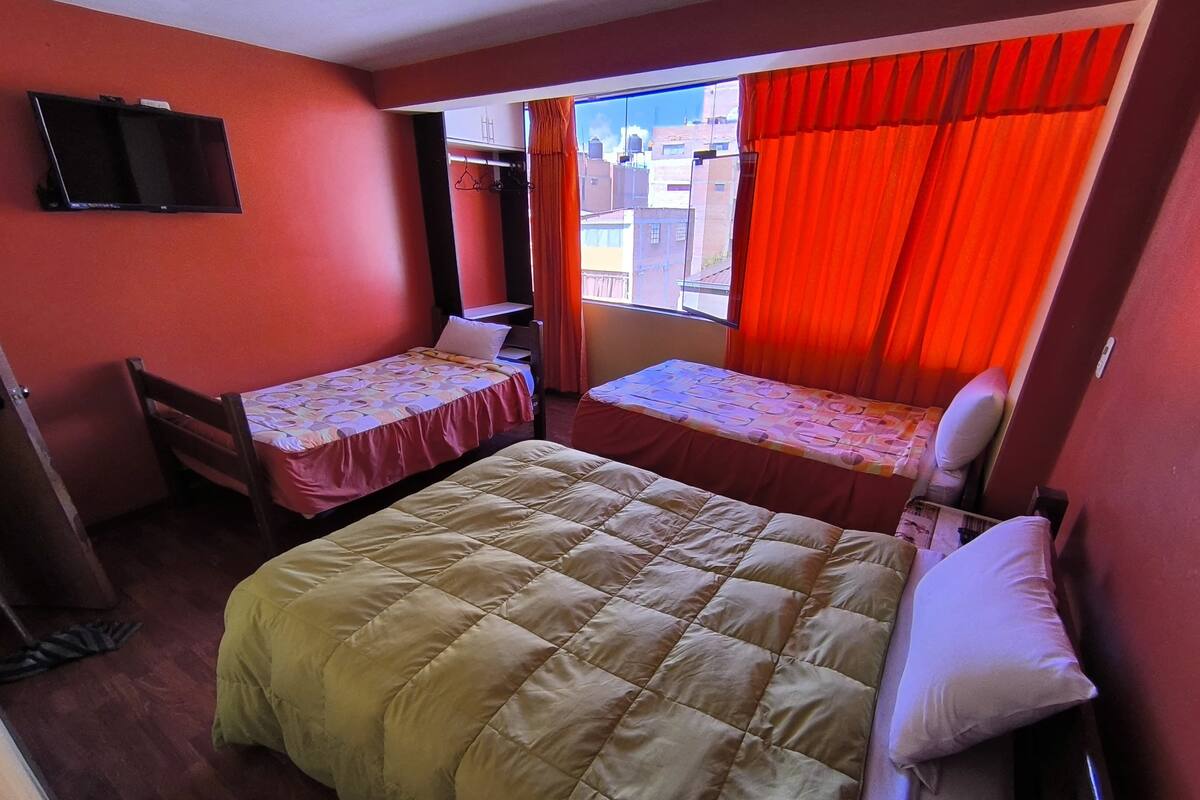 A room with a large bed, two smaller beds, a TV, and a window with curtains.