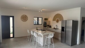 Eine moderne Küche mit einer zentralen Kochinsel, weißen Barhocker, einem großen Kühlschrank und einem dekorativen Ventilator.