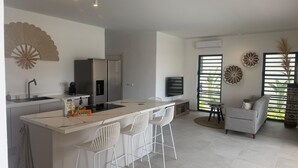 Eine moderne Küche mit Kochinsel, weißen Barhocker, einem Essbereich mit einer Couch und dekorativer Wandgestaltung.