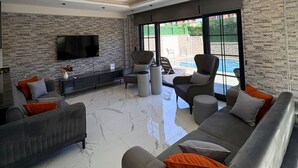 Un salón moderno con una pared de piedra, un televisor de pantalla plana y vistas a una piscina.