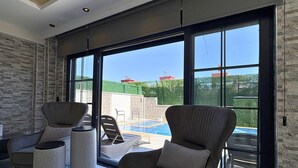 Una sala de estar moderna con vistas a la piscina, ventanas amplias y una pared de piedra.