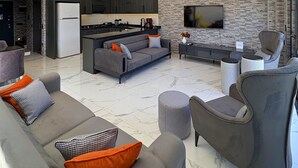 Una sala de estar moderna con un sofá, sillones, televisor y una zona de cocina.