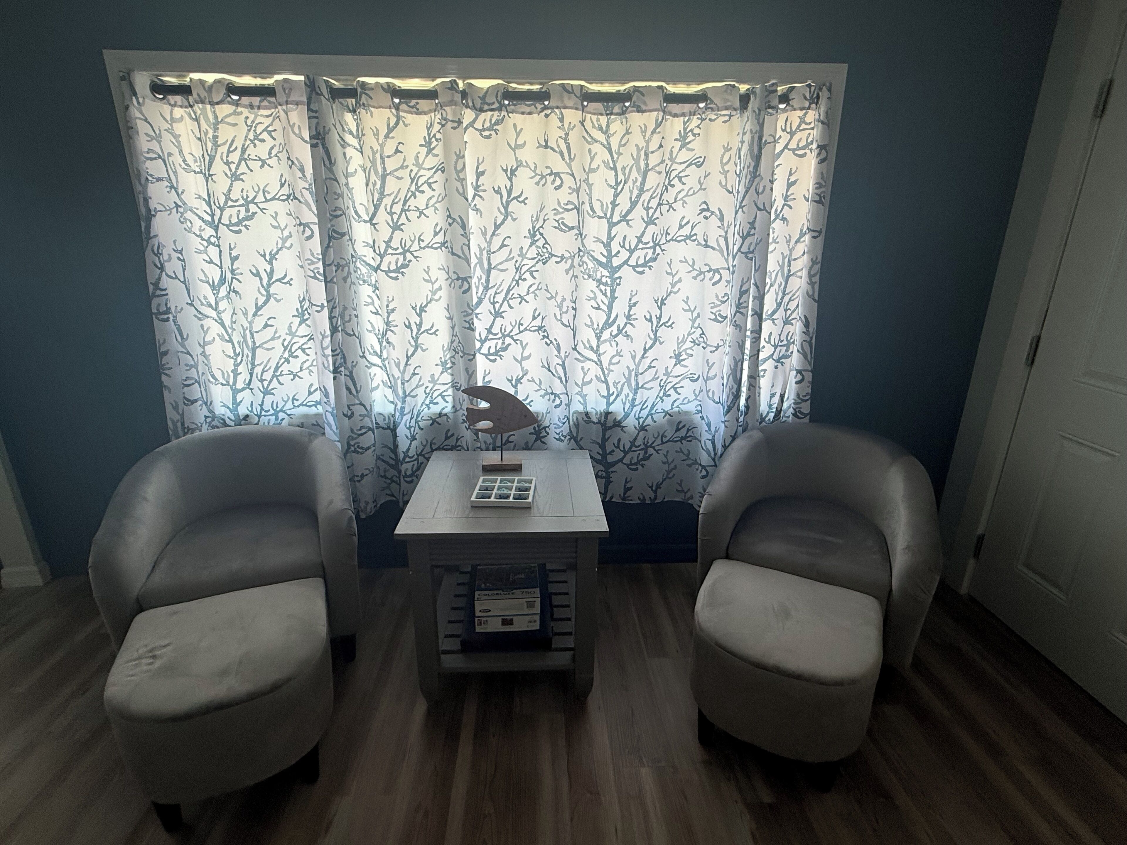 Une pièce avec deux chaises, une petite table et une fenêtre ornée de rideaux à motifs.