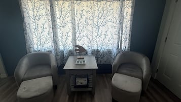 Une pièce avec deux chaises, une petite table et une fenêtre ornée de rideaux à motifs.
