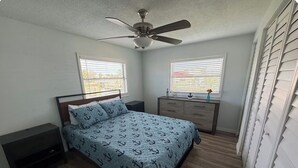 A bedroom with a bed, nightstands, a dresser, a ceiling fan, and two windows with blinds. - Cozy 2-bedroom house in peaceful Hudson on a canal (Hudson)