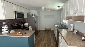 Une cuisine avec des meubles blancs, un four à micro-ondes, un réfrigérateur, une cuisinière et un ventilateur de plafond.
