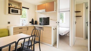 Una cucina compatta con forno a microonde, piano cottura e lavello, una zona pranzo con sedie, e un letto in una stanza adiacente.