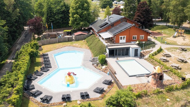 Una proprietà residenziale con piscina, lettini prendisole, area giochi e una grande casa con garage.