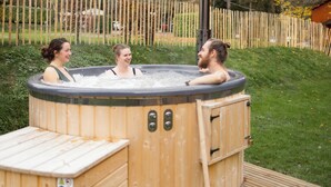 Ein hölzernes Whirlpool mit Leiter, umgeben von einer Holzumzäunung und viel Grün.