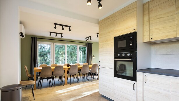 Eine moderne Küche mit Holzausstattung, ein Essbereich mit Stühlen und ein großes Fenster.