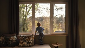 Ein Kind steht an einem Fenster mit Blick auf Bäume.