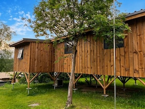 Een houten boomhuis met één raam aan de linkerkant, ondersteund door metalen poten.