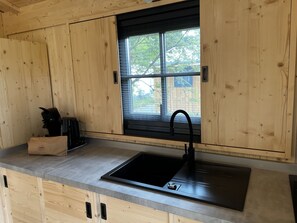 Een keuken met houten kastjes, een zwarte spoelbak en een raam met zonwering.