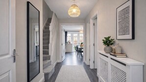 Um corredor com escadaria, um console branco com objetos decorativos, um espelho grande e um lustre.