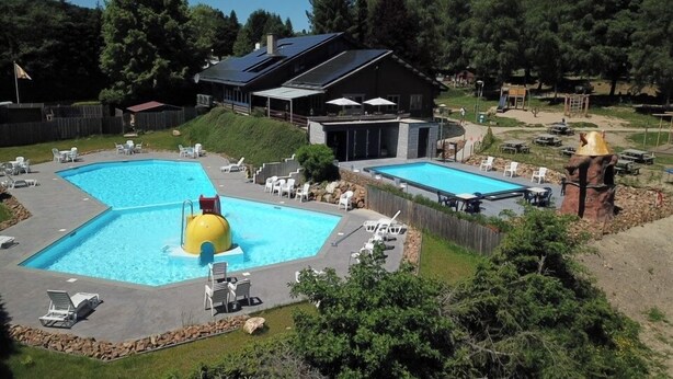 Et poolområde med to pools, liggestole og en bygning med et mørkt tag.