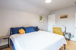 Un dormitorio con una cama, una silla, una mesita de noche y un cuadro colgado en la pared.
