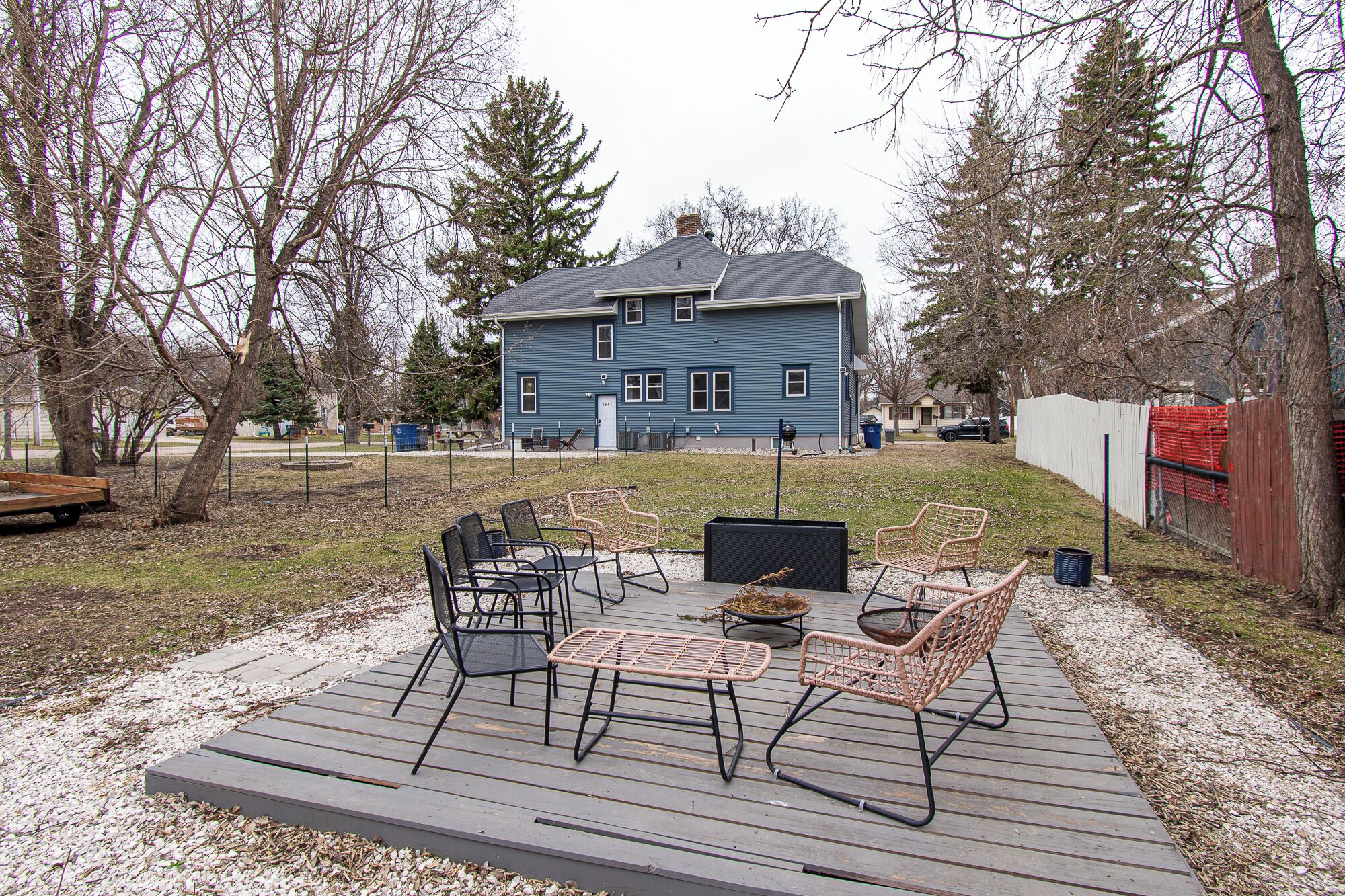 Ein blaues Haus mit Terrasse, Gartenmöbeln und einem umzäunten Hof.