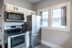 Una cocina compacta con microondas, estufa, refrigerador y dos ventanas.