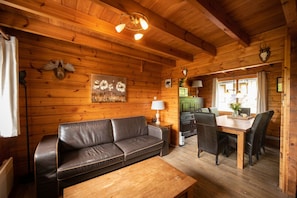 L’intérieur d’un chalet accueillant, avec un plafond en bois, un canapé, une table à manger avec des chaises et une cheminée.